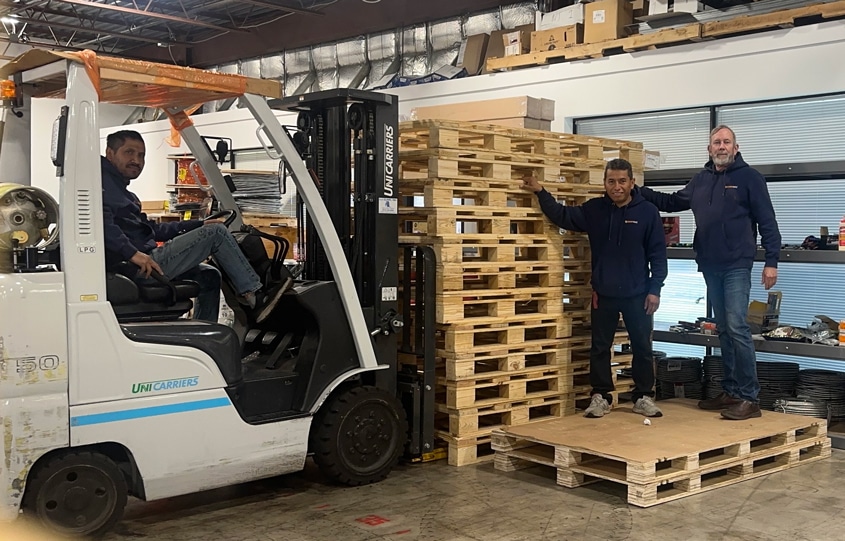SunnyMac employees standing by pallets and a forklift